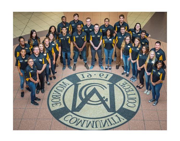 Group photo of MCC Housing & Residence Life team around the MCC crest in the Brighton campus Atrium floor